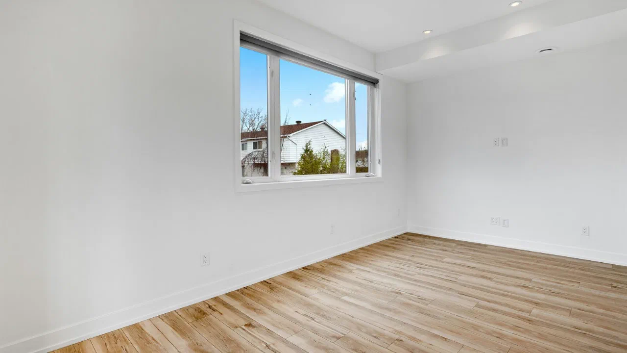 An empty room with a bare wood floor and a window looking onto trees